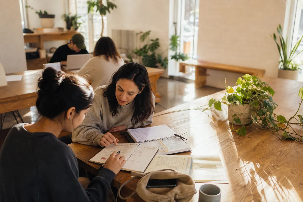 A university student and tutor use feedback and a planner to set weekly study goals at a community-centre table.